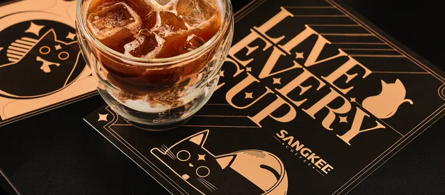 Iced coffee on a SANGKEE mat featuring Cafemi cat illustrations and Live Every Purr typography